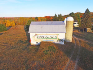 image of a white barn with Leelanau painted on its side with a silo and autumn leaved trees in background